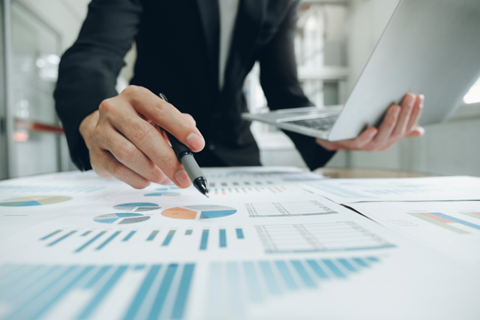 Person writing on financial metric sheets and holding a laptop